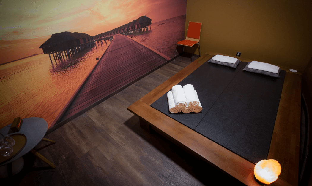 Sauna Ganbanyoku, dwa miejsca leżące z ręcznikami i poduszkami, obraz długiego mola na morzu na ścianie