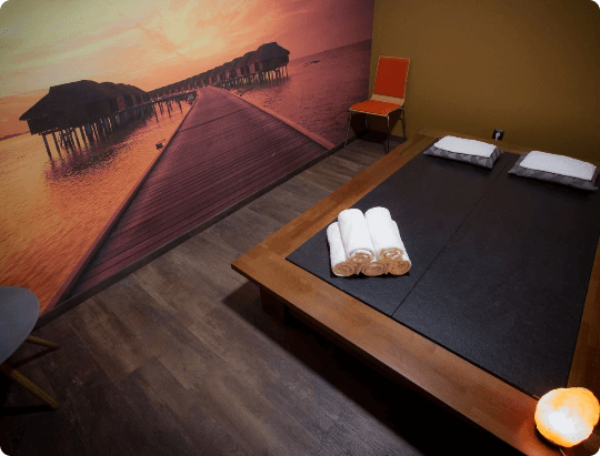 Sauna Ganbanyoku, dwa miejsca leżące z ręcznikami i poduszkami, obraz długiego mola na morzu na ścianie
